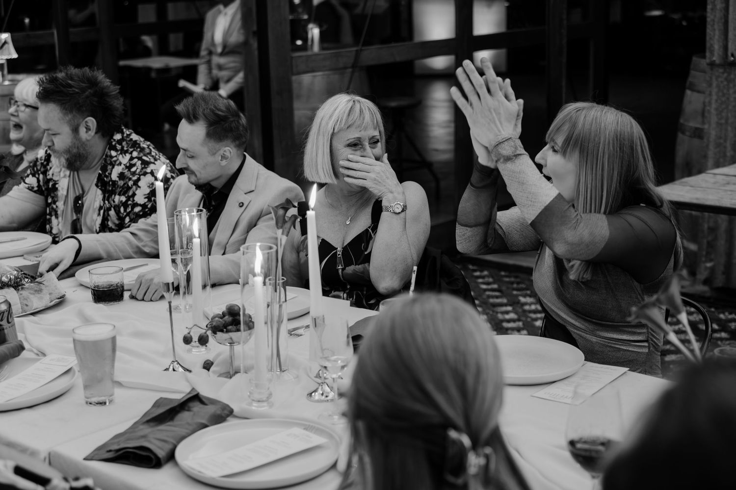 Black and white photo of guests reacting with surprise at a candlelit dinner party table.