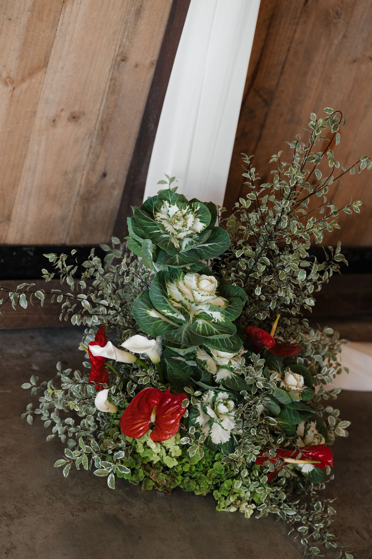 Rustic floral arrangement with red anthuriums, white roses, and eucalyptus greenery against a wooden barn backdrop.