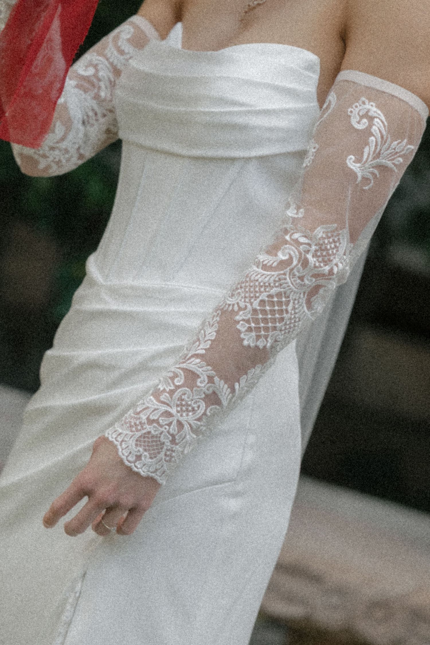 Bride wearing a strapless white satin gown with elegant sheer lace gloves featuring floral embroidery.