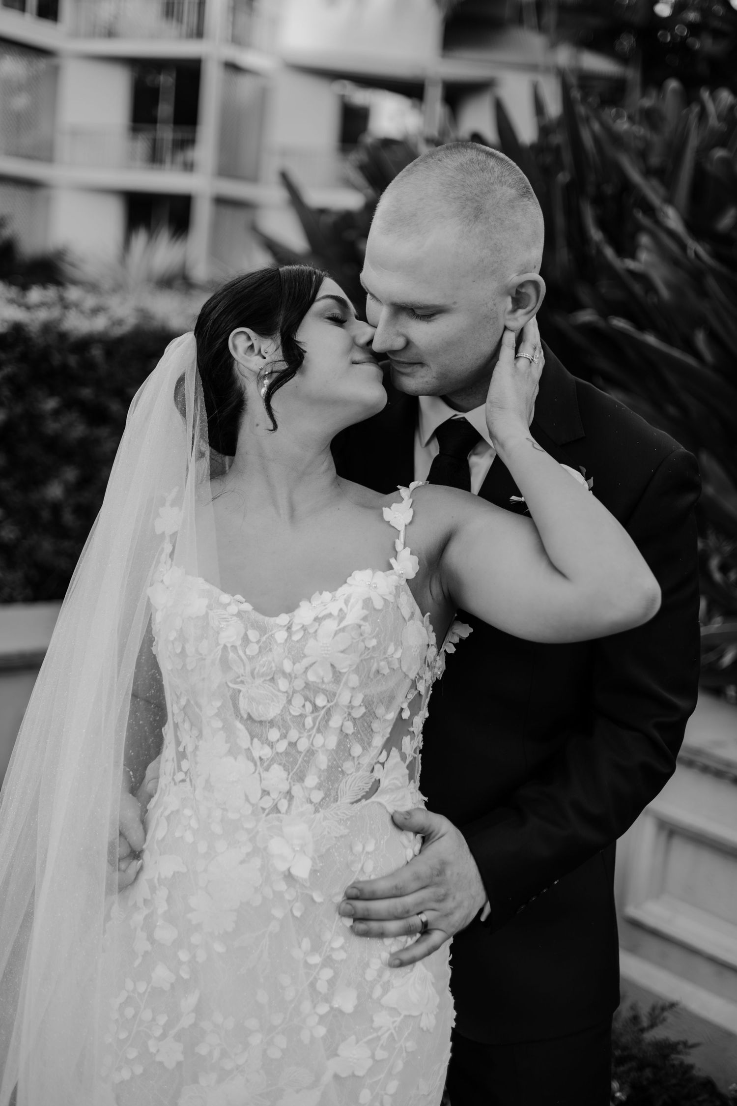 A tender black and white wedding photo shows a couple sharing an intimate moment in formal attire.