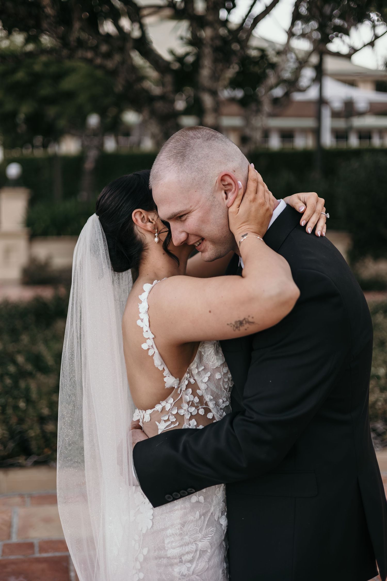 A romantic wedding couple shares intimate kisses while wearing traditional formal attire in an outdoor garden setting.