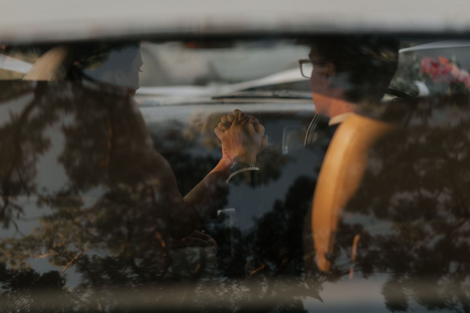 Person visible through car window with reflections of trees in golden hour light.