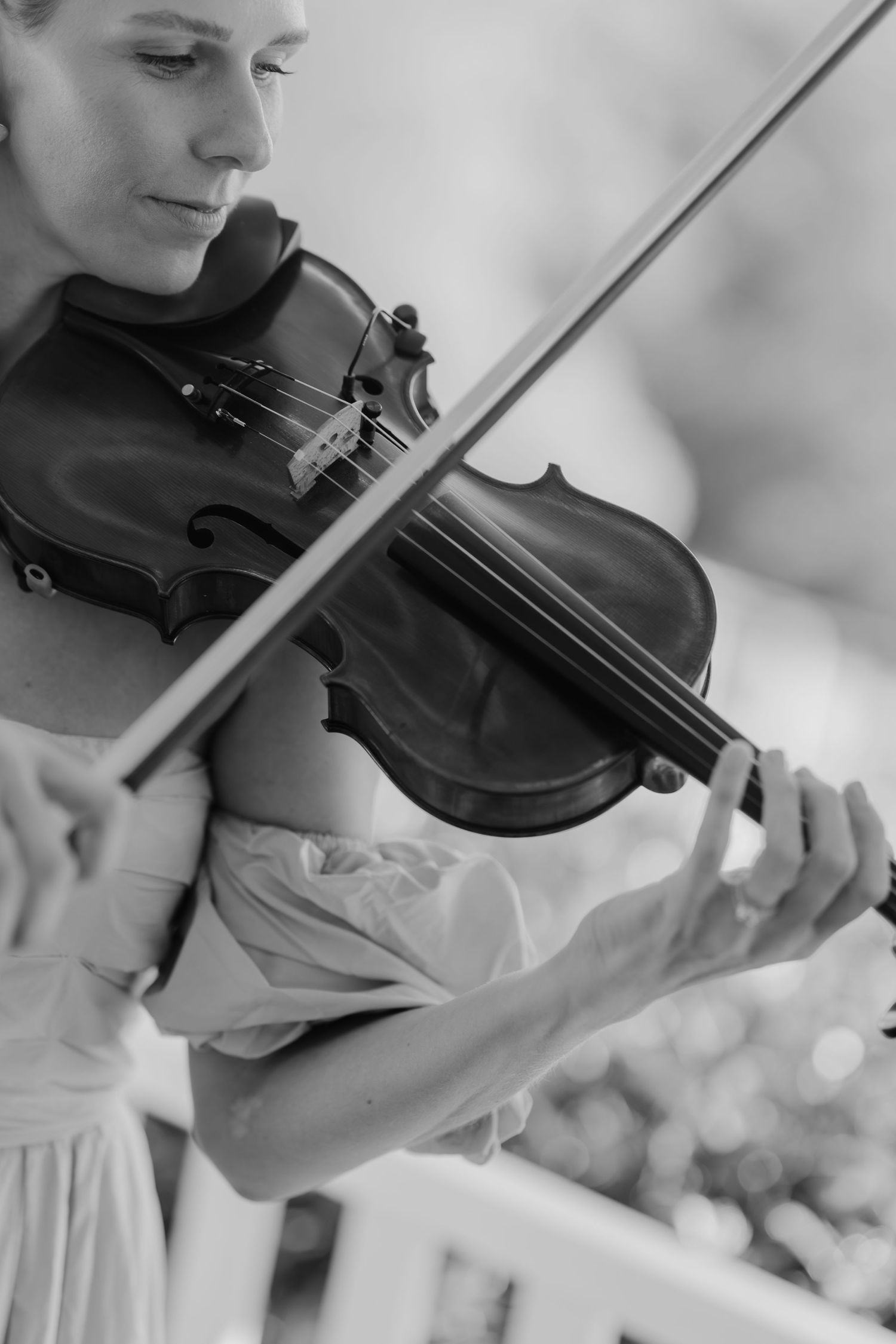 Black and white photo of a woman in a dress playing violin outdoors, captured in an elegant musical performance.