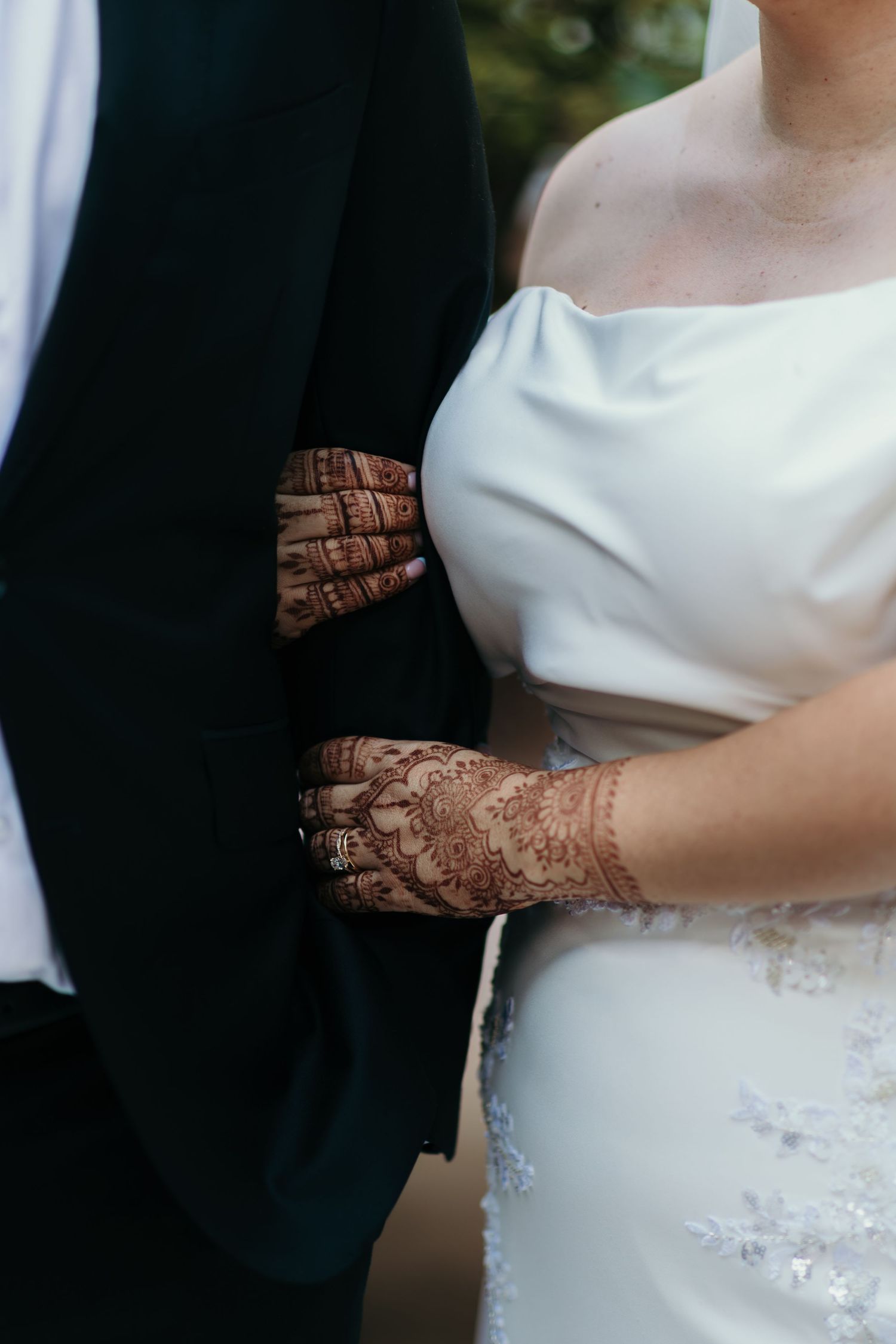 Close-up detail of intricate henna designs on hands against a white wedding dress with delicate lace embellishments.