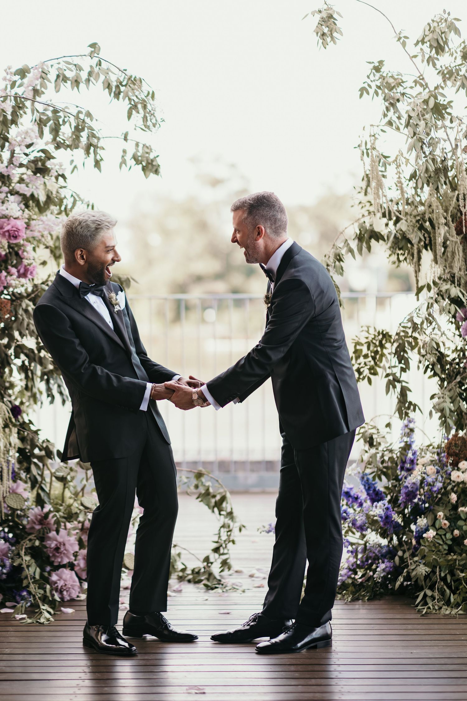 Emotional wedding moment between family members surrounded by purple and pink floral arrangements.