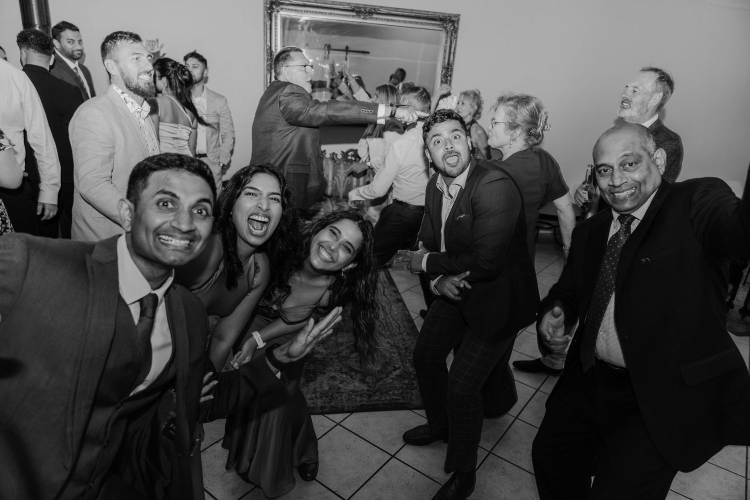 Black and white photo of a joyful group posing for a selfie at a lively wedding reception party.