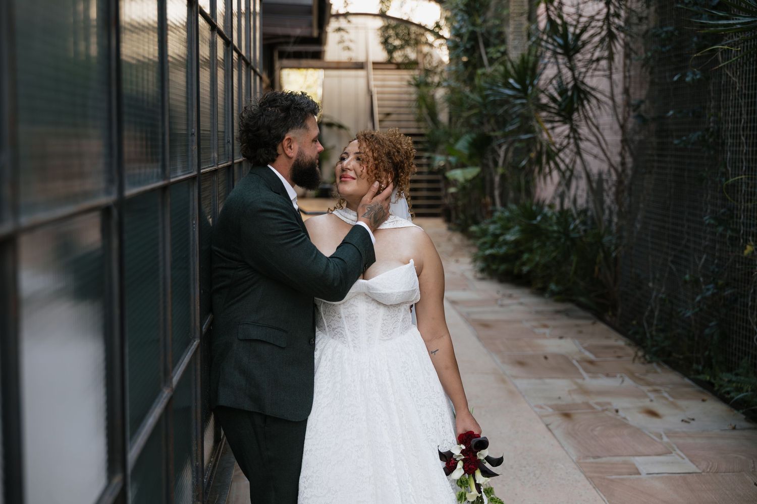 A bride in a white gown and groom in a dark suit share a romantic moment in an outdoor courtyard.