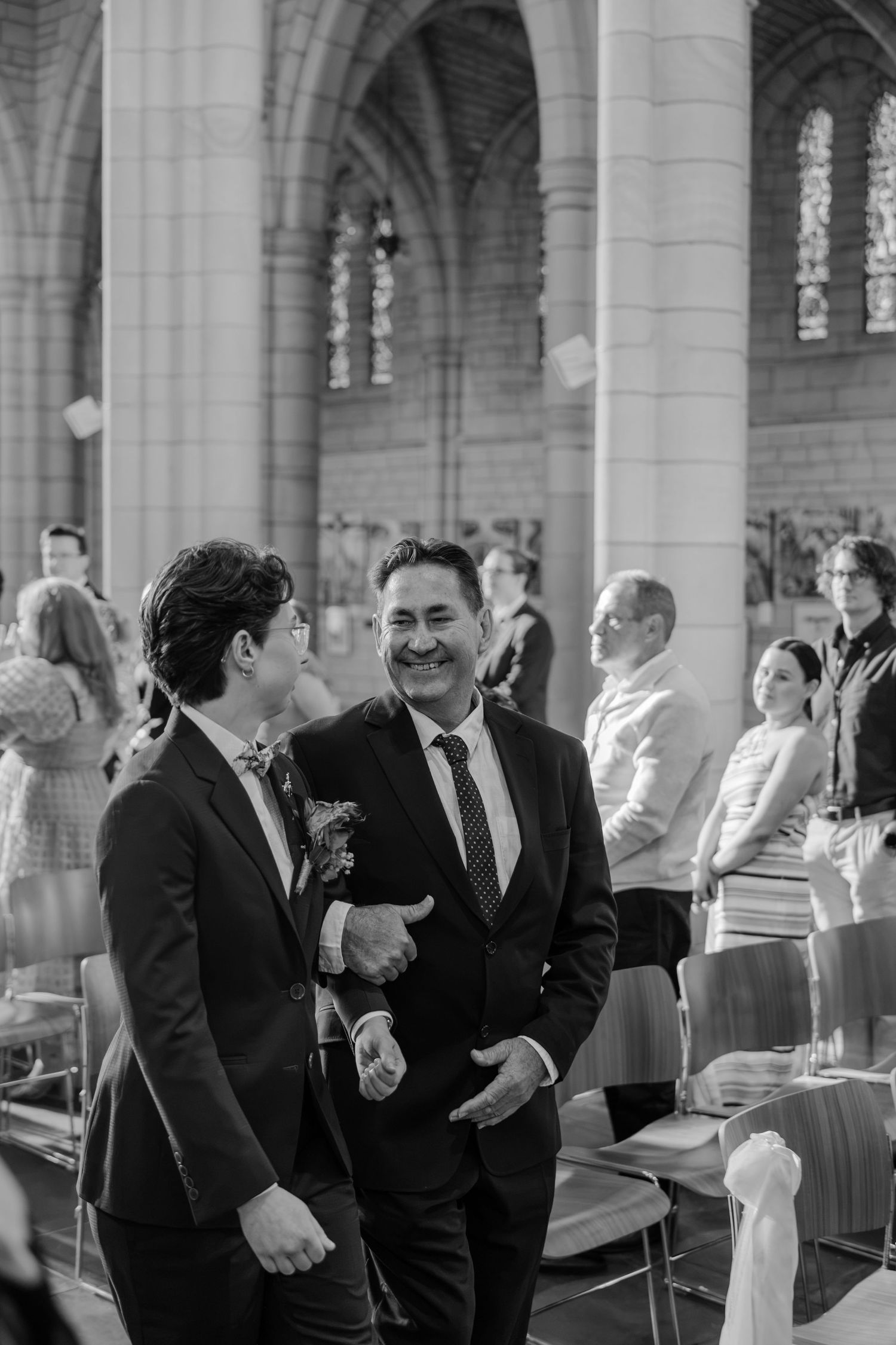 Two men in suits share a joyful moment during a wedding ceremony inside a grand church.