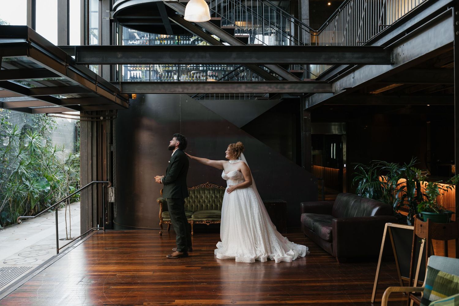 Bride and groom share a romantic first dance in an elegant industrial venue with dark walls and warm hardwood floors.