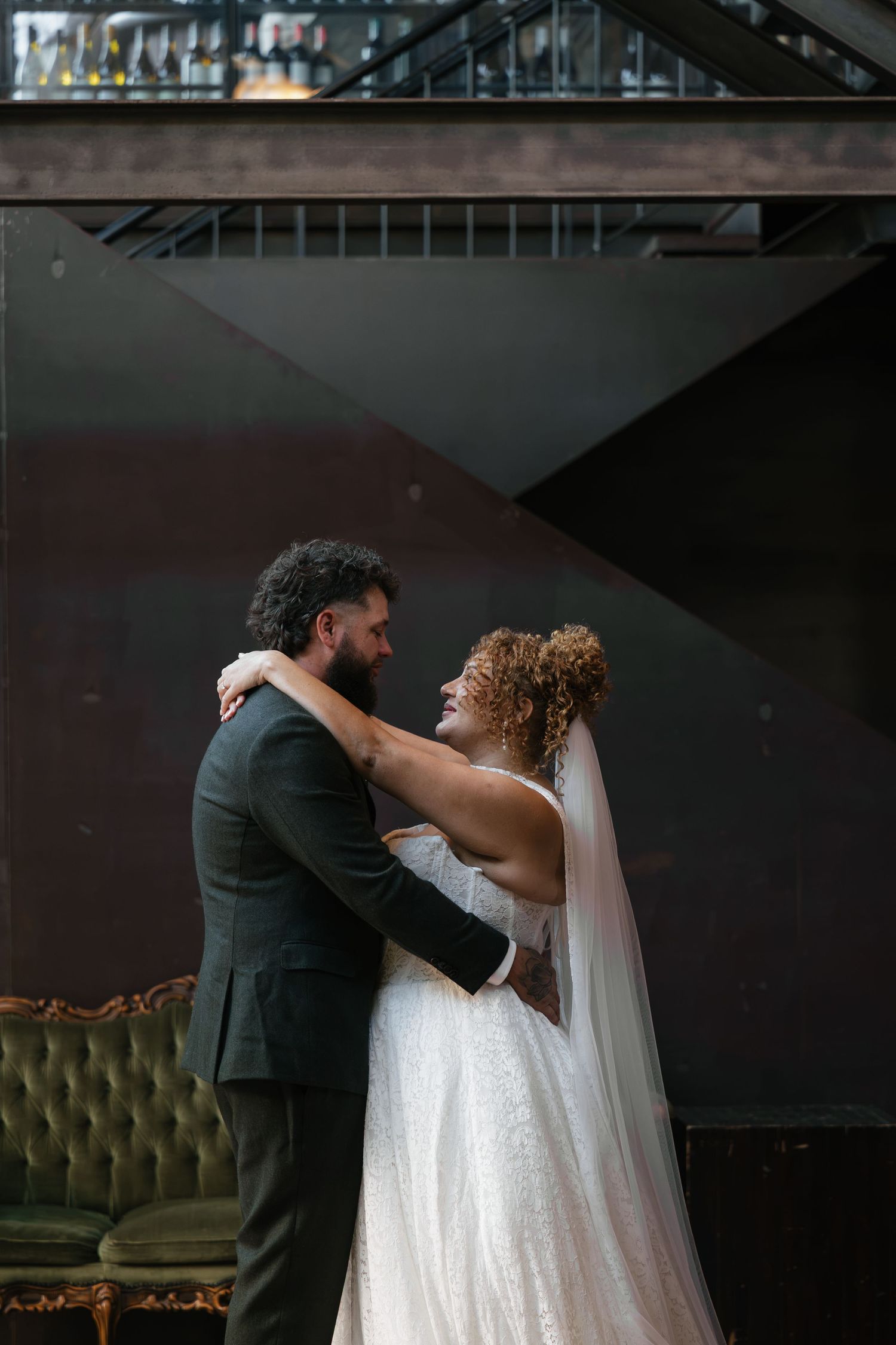 A bride and groom share a romantic embrace, smiling at each other in an elegant indoor wedding venue.