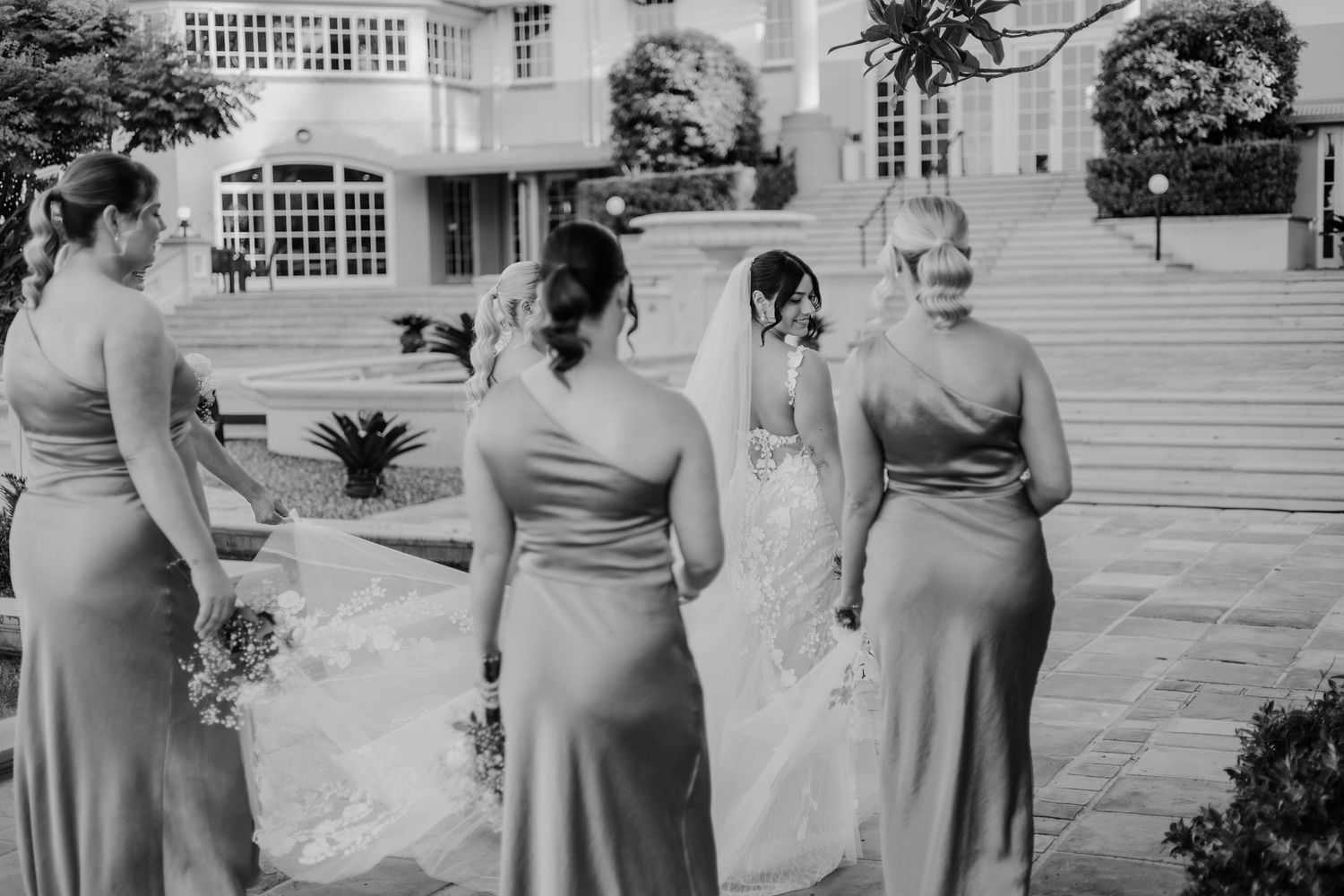 Black and white photo showing wedding party members lined up outdoors at an elegant venue.