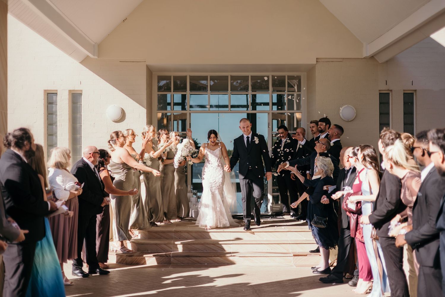 Wedding guests line a bright hallway waiting to greet the newlyweds during a receiving line at a formal ceremony.