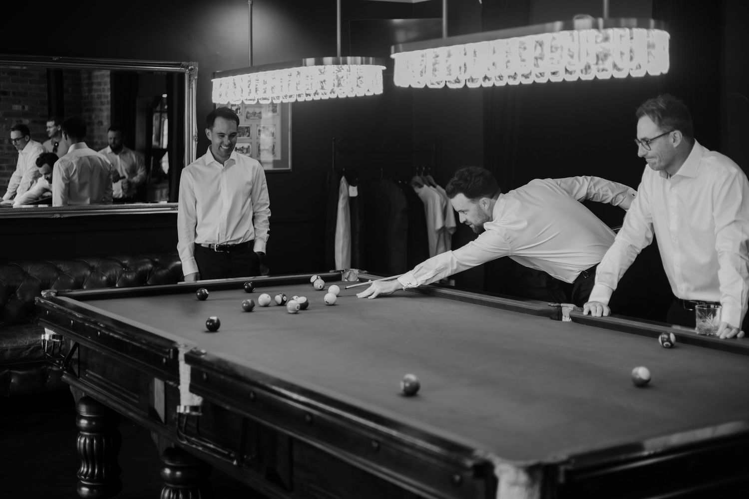 Men playing pool billiards in a stylish bar, black and white photo of friends enjoying a game.