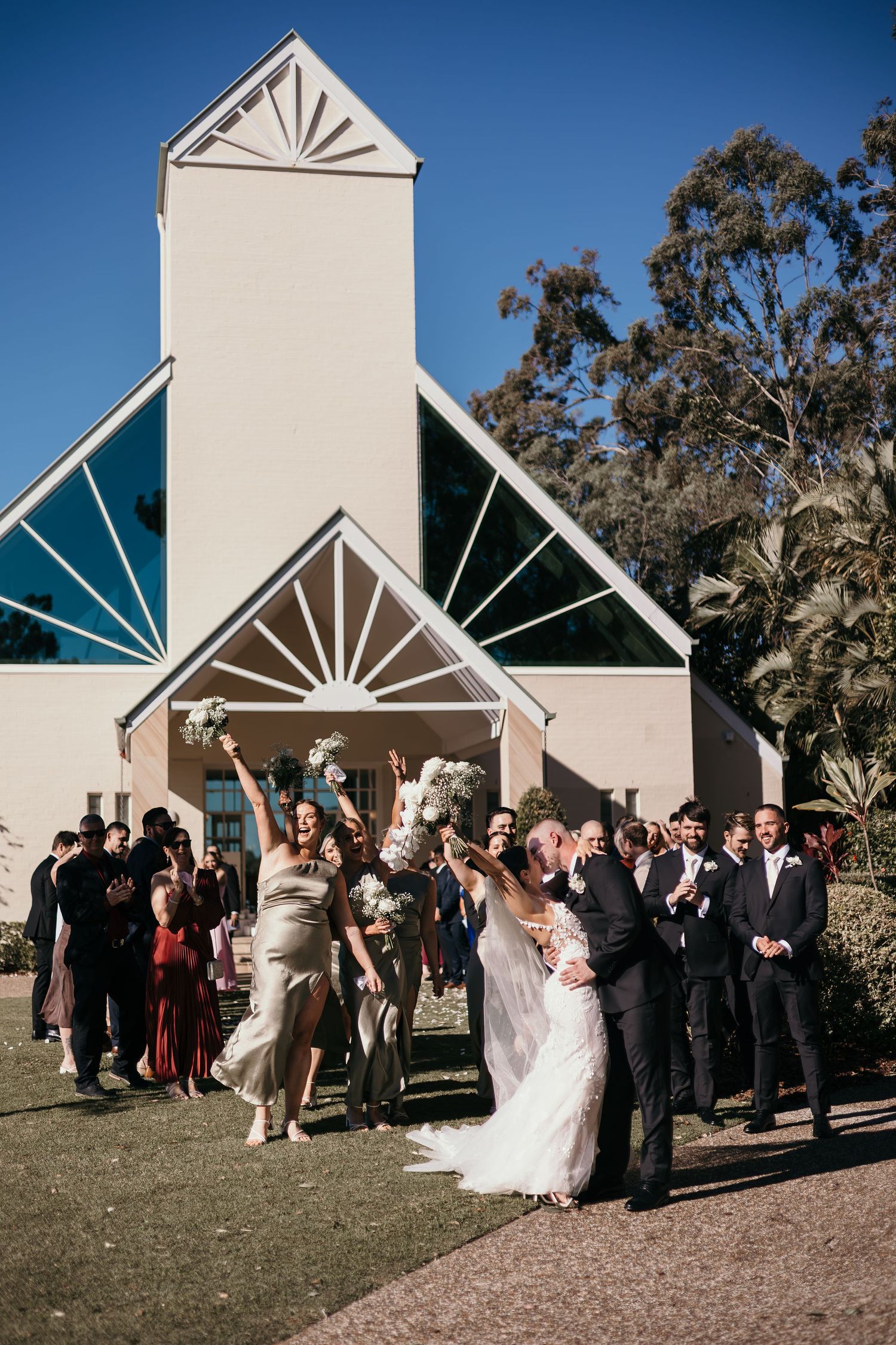 Wedding party gathers outside a modern church with distinctive geometric architectural details and sunburst window designs.