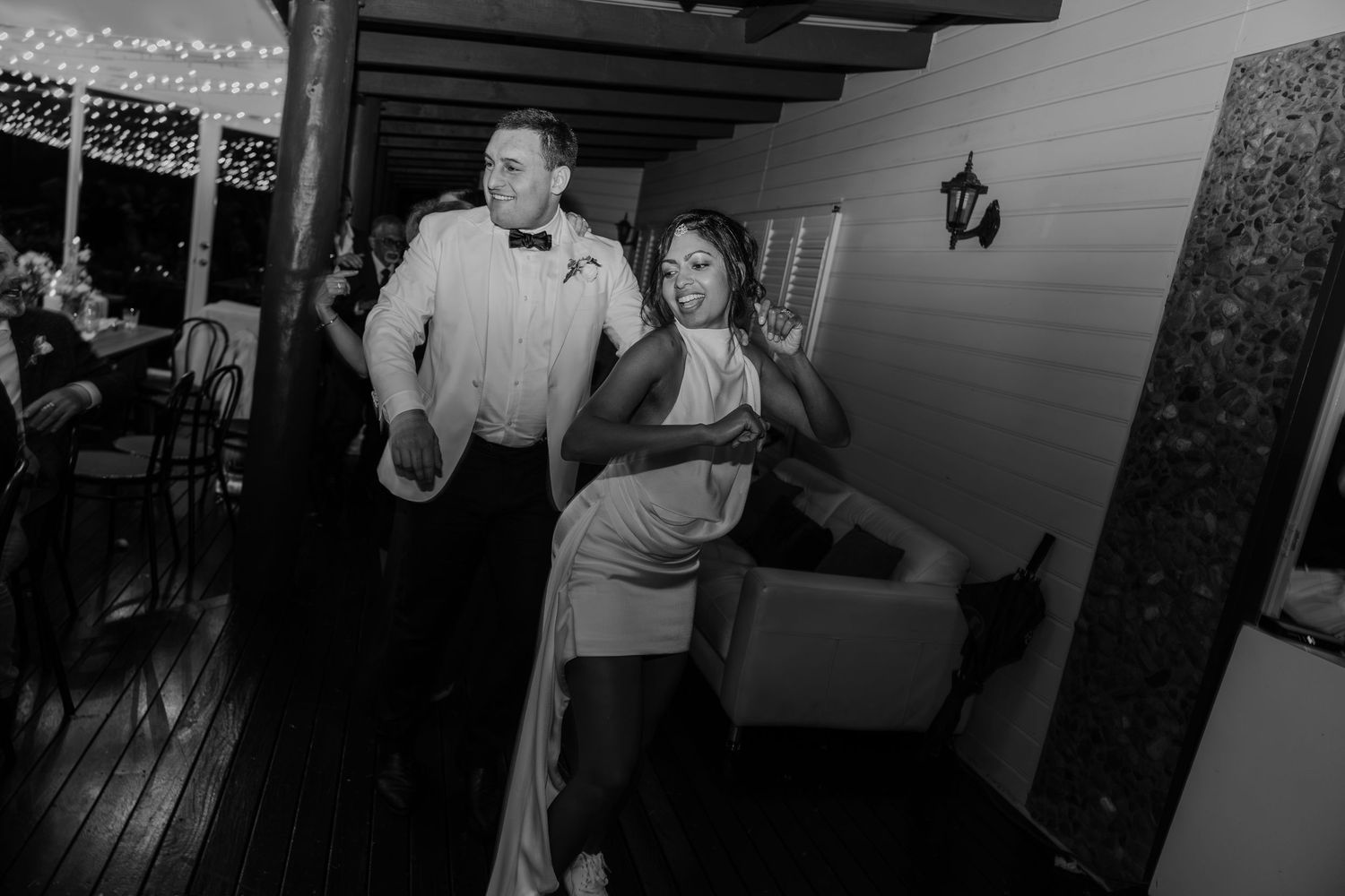 A couple dances energetically at a wedding reception on a decorated outdoor deck in this black and white photo.