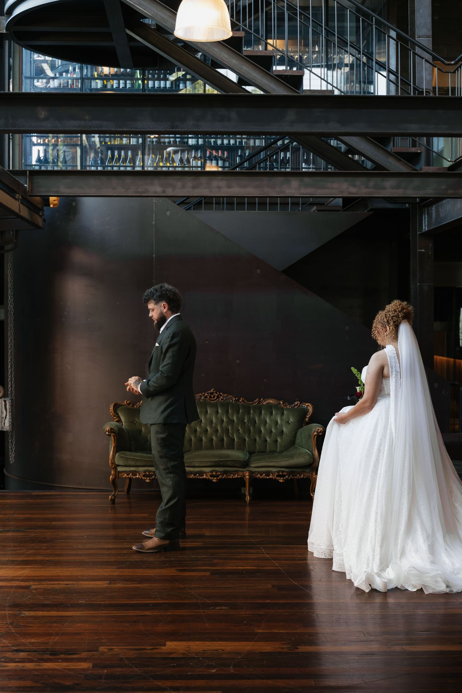 Bride in white gown and groom in dark suit share a first look moment in an elegant venue with green velvet sofa.
