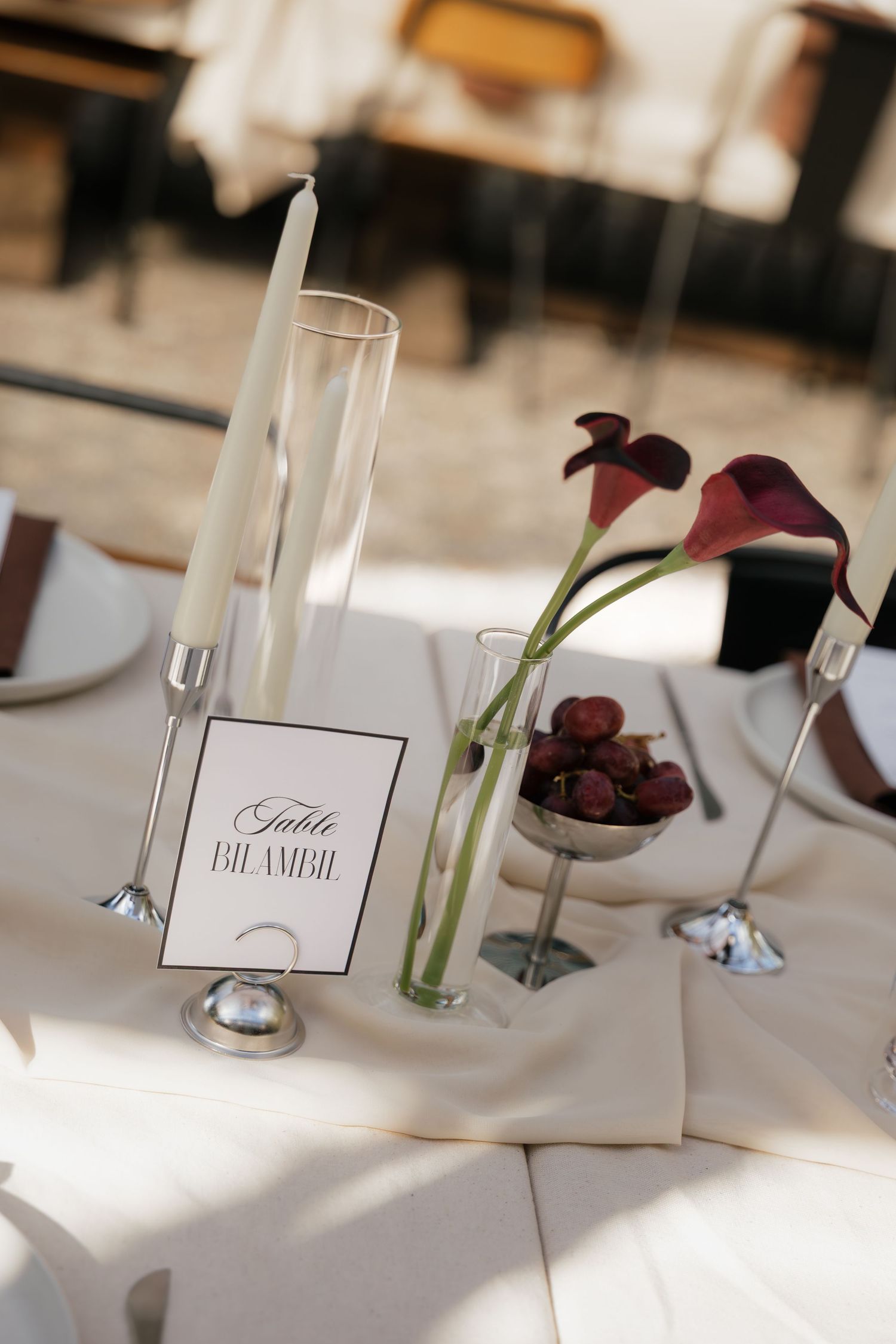 Elegant wedding table setting with dark calla lilies, white candle, champagne flute, and a decorative table number card.
