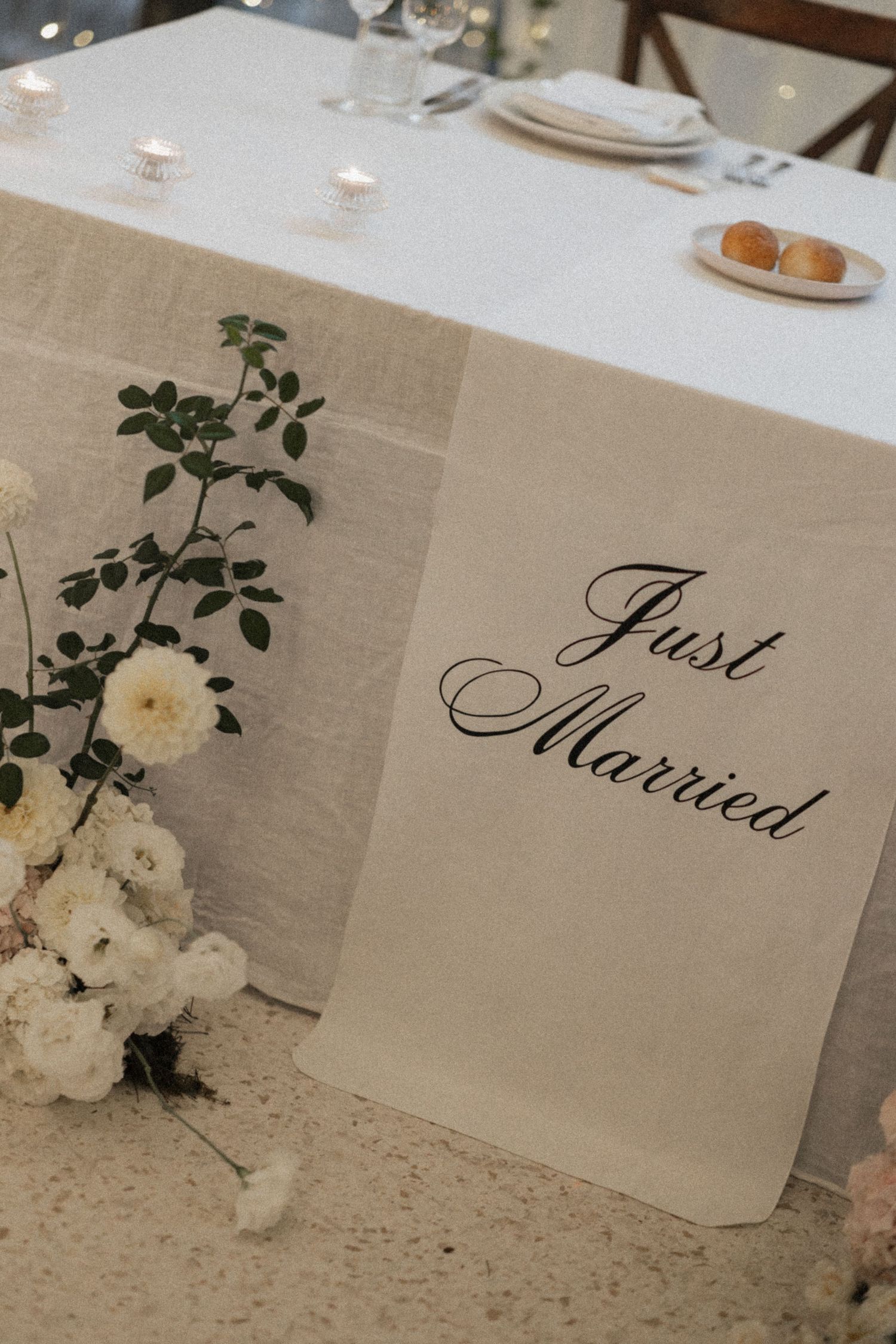 A elegant wedding reception table with a Just Married sign, white floral arrangements, and candles on a linen tablecloth.