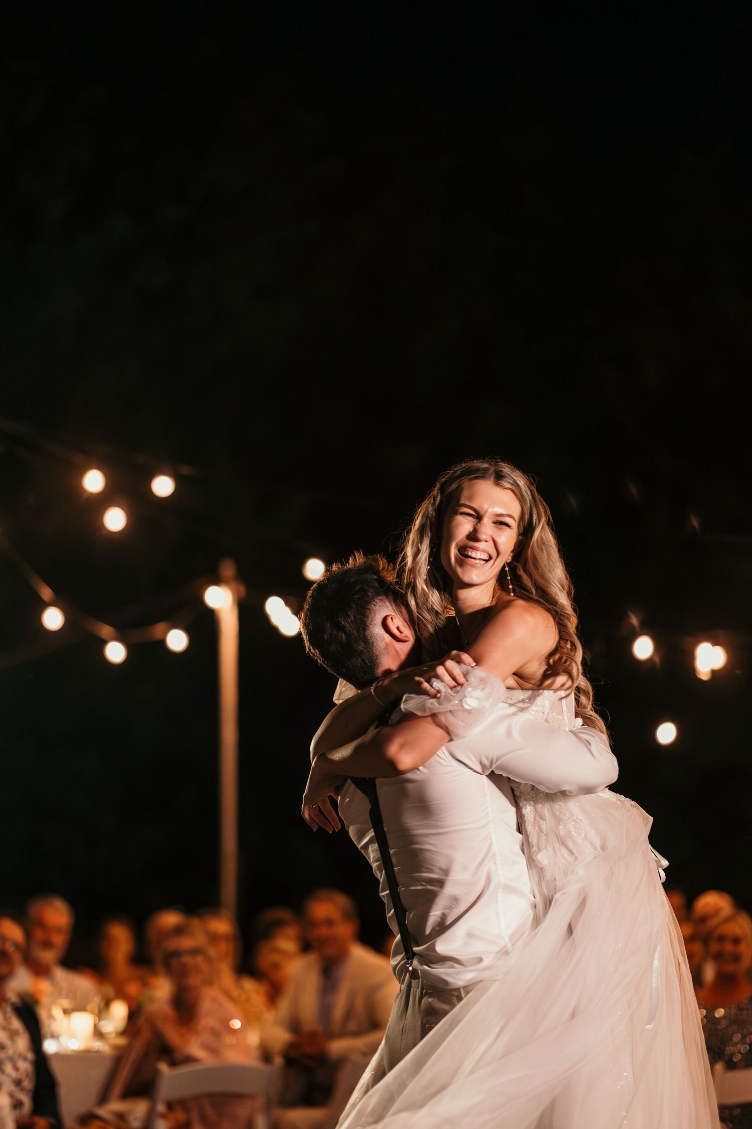 Joyful dance moment captured at night wedding celebration with string lights in background.