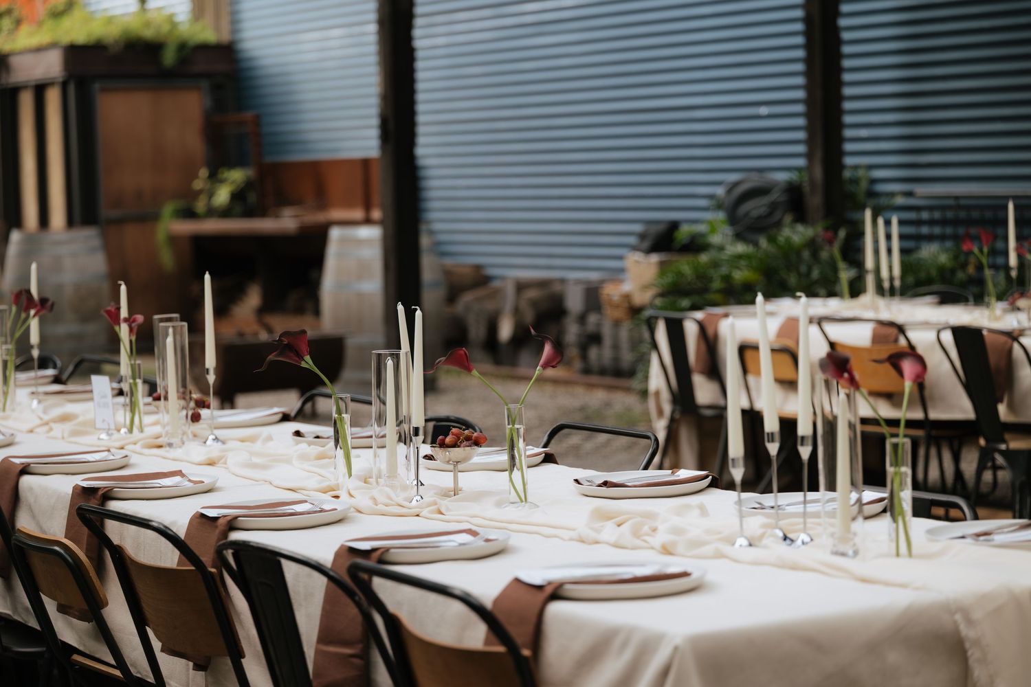 Elegant outdoor dining table set with white linens, candles, and wine bottles for a rustic event.