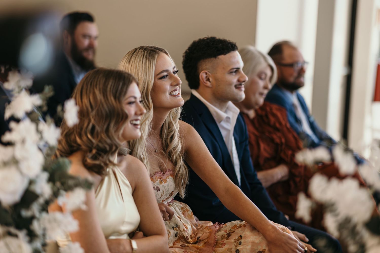 Wedding guests seated in rows laugh joyfully during a ceremony celebration.