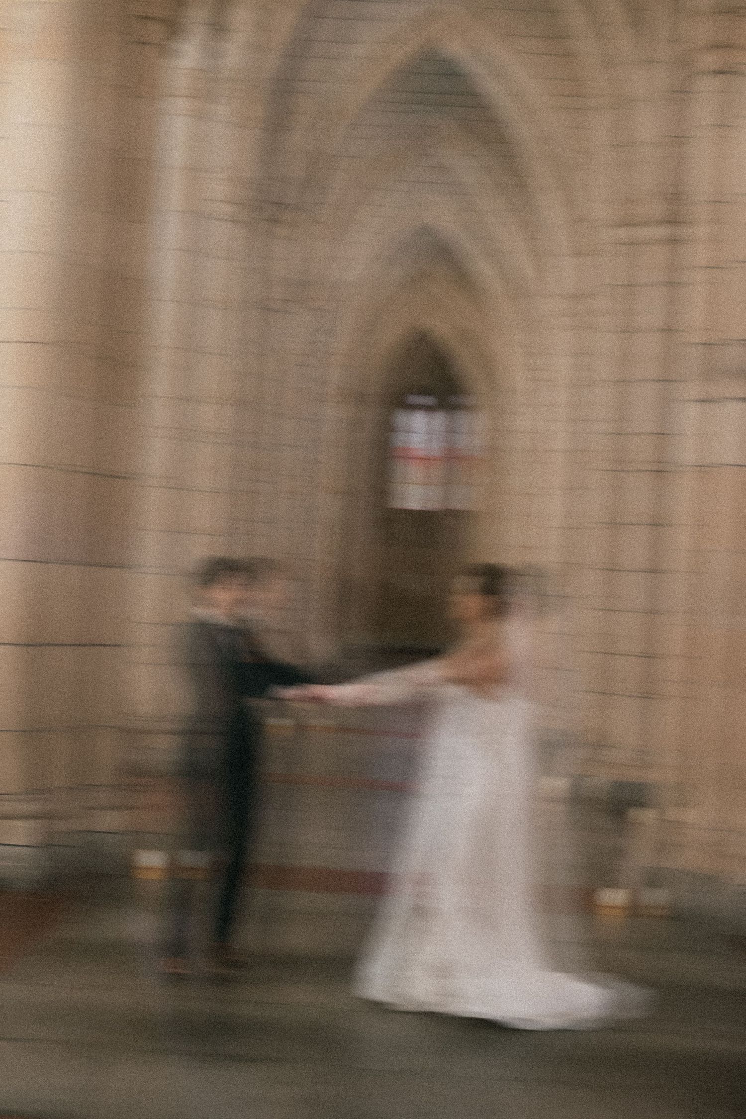 Blurry motion photo of a bride and groom holding hands inside a gothic stone church during their wedding ceremony.