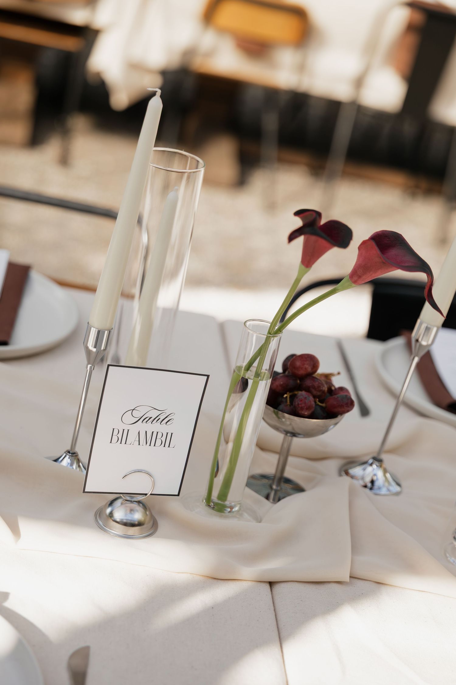 Elegant wedding table setting with calla lilies, white candle, grapes, and a table number card on white linen.