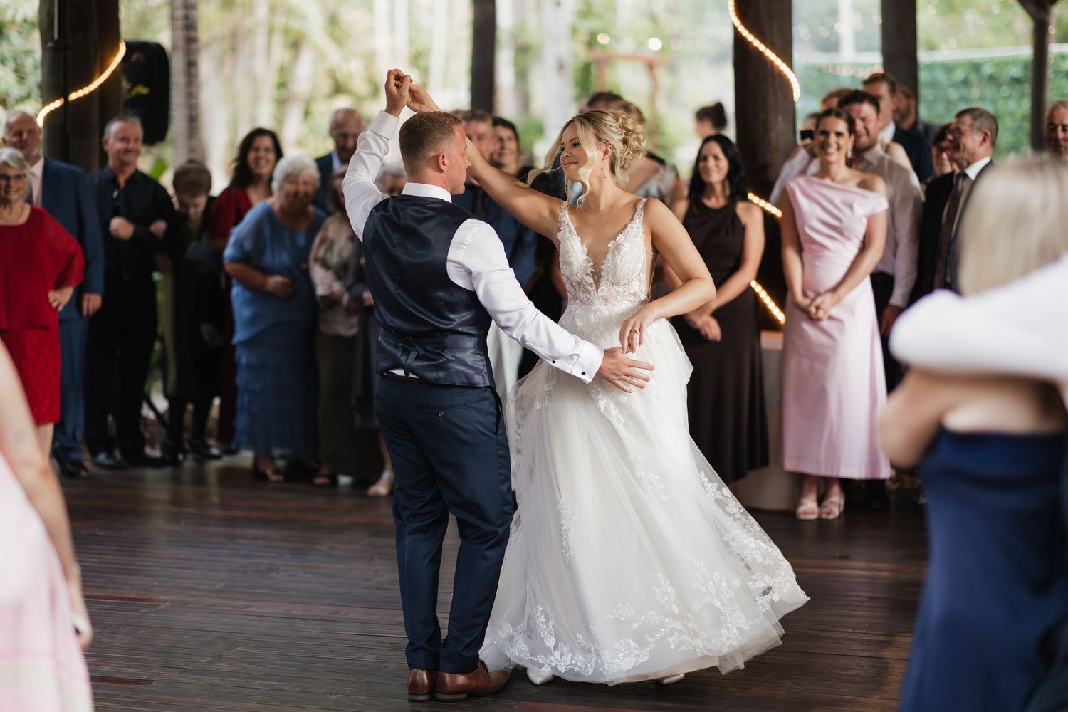 Bride and groom share their first dance surrounded by wedding guests at an elegant indoor venue.