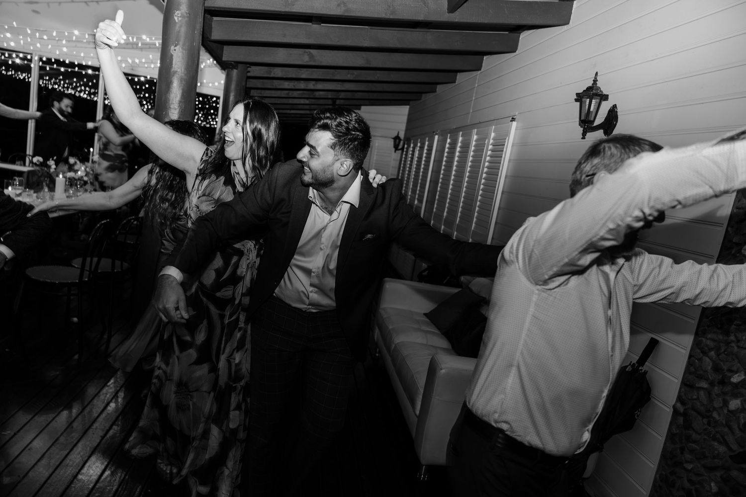 Black and white photo of guests dancing joyfully at a wedding reception party indoors.