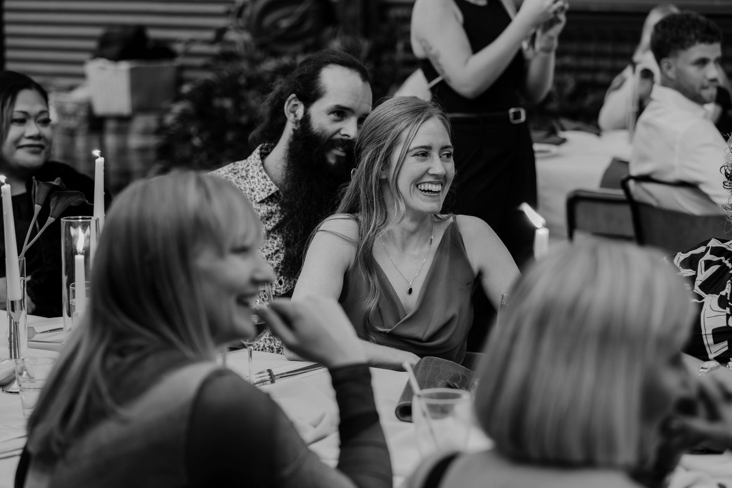 Black and white photo of guests laughing and enjoying themselves at a wedding reception dinner table.