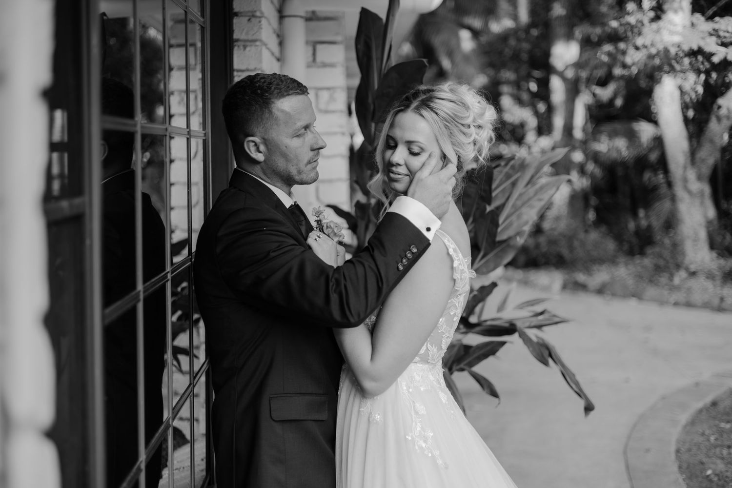 Black and white photo of a bride and groom sharing a tender moment outside a brick building on their wedding day.