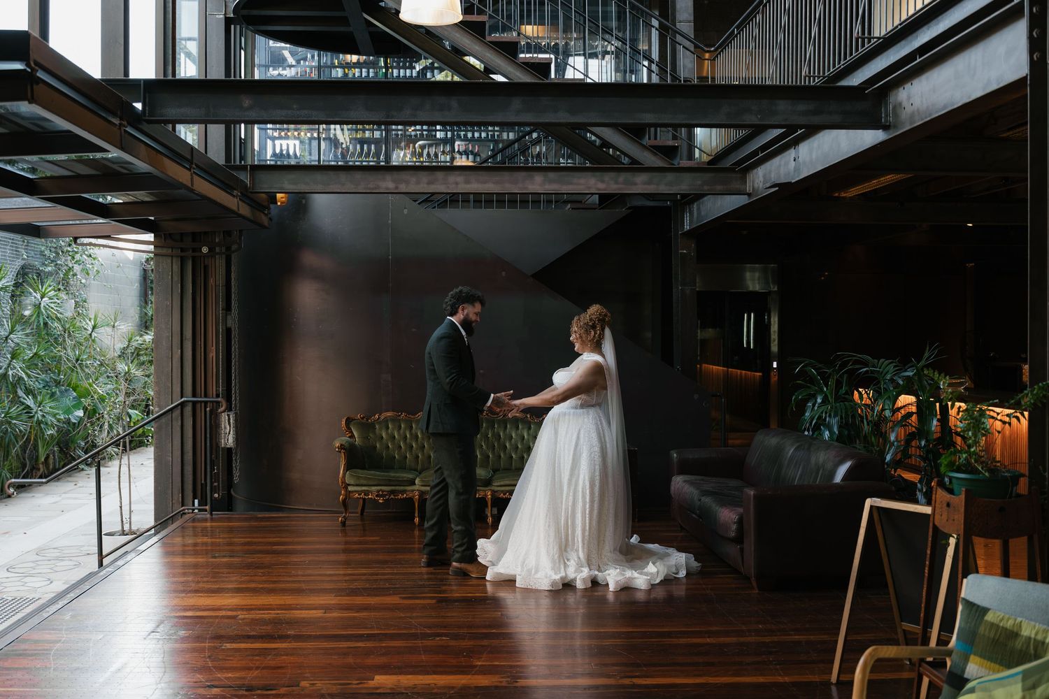 Bride and groom share a romantic first look moment in a modern industrial wedding venue with dark walls and wooden floors.