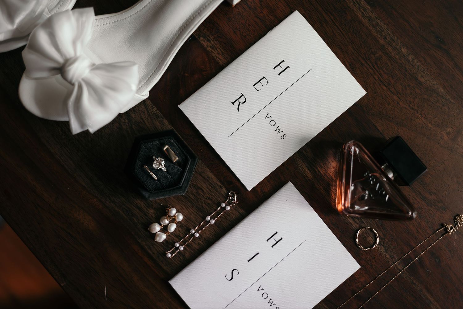 Close-up of wedding vow books with rings, earrings, and bridal accessories arranged on a dark wooden surface.