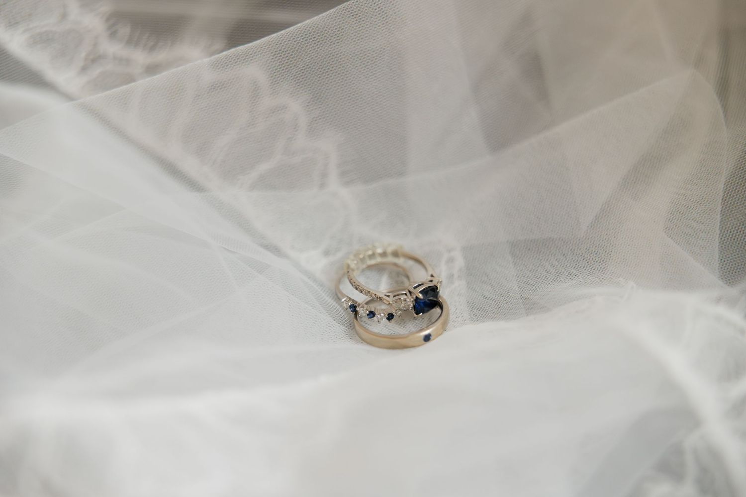 Wedding rings with sapphire and diamond details resting on a white bridal veil.