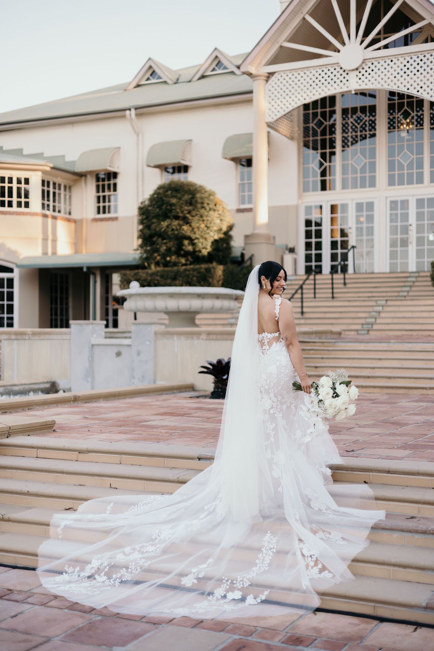 A stunning bridal portrait series on elegant stone steps showcasing a flowing lace wedding gown and cathedral veil.