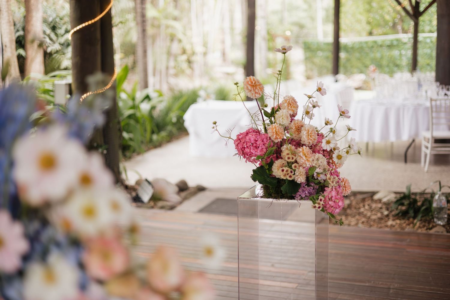 Elegant wedding venue with pink floral arrangements, white table settings, and lush greenery in a garden setting.