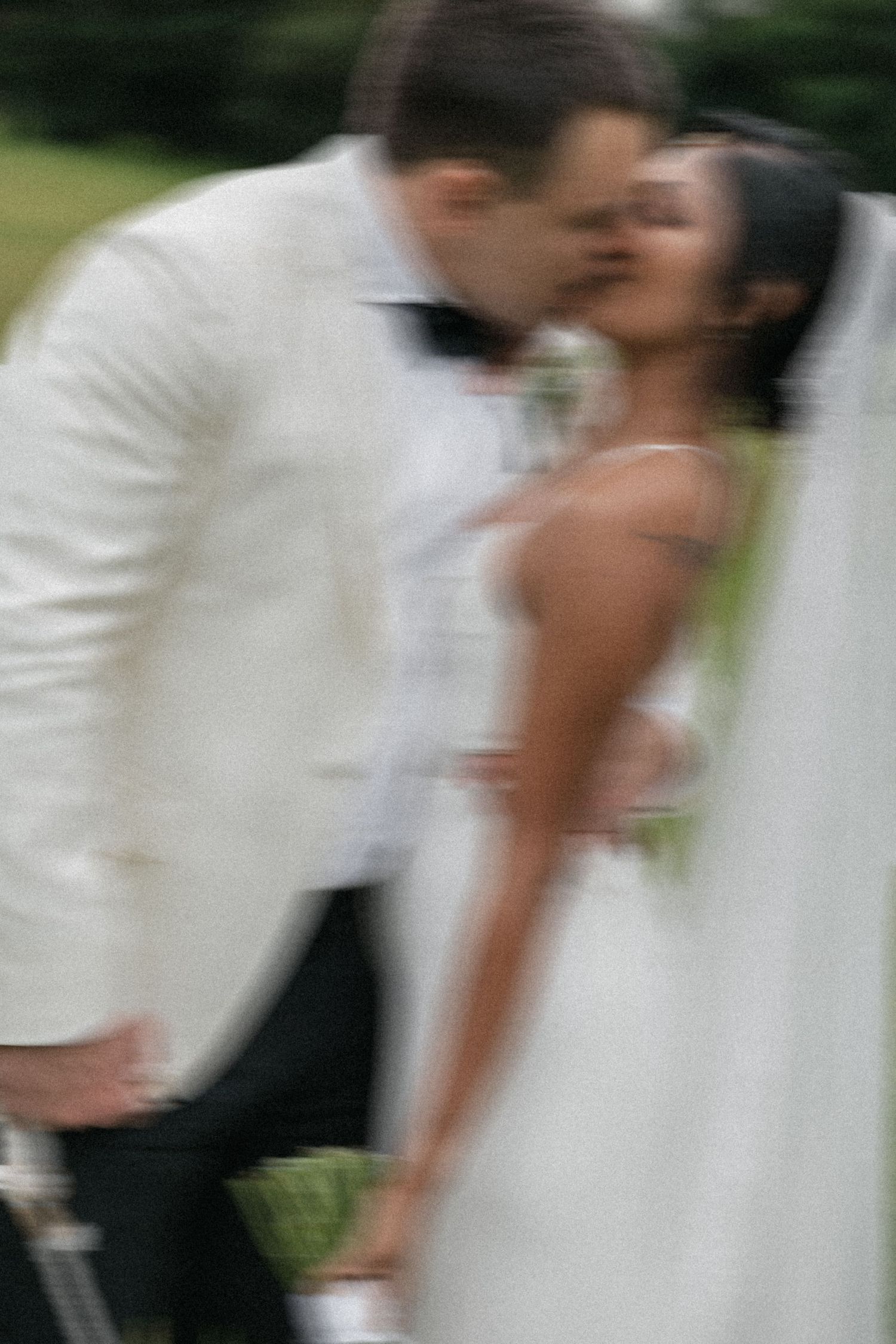 Blurred romantic photo of a bride and groom sharing a kiss outdoors, wearing white wedding attire.