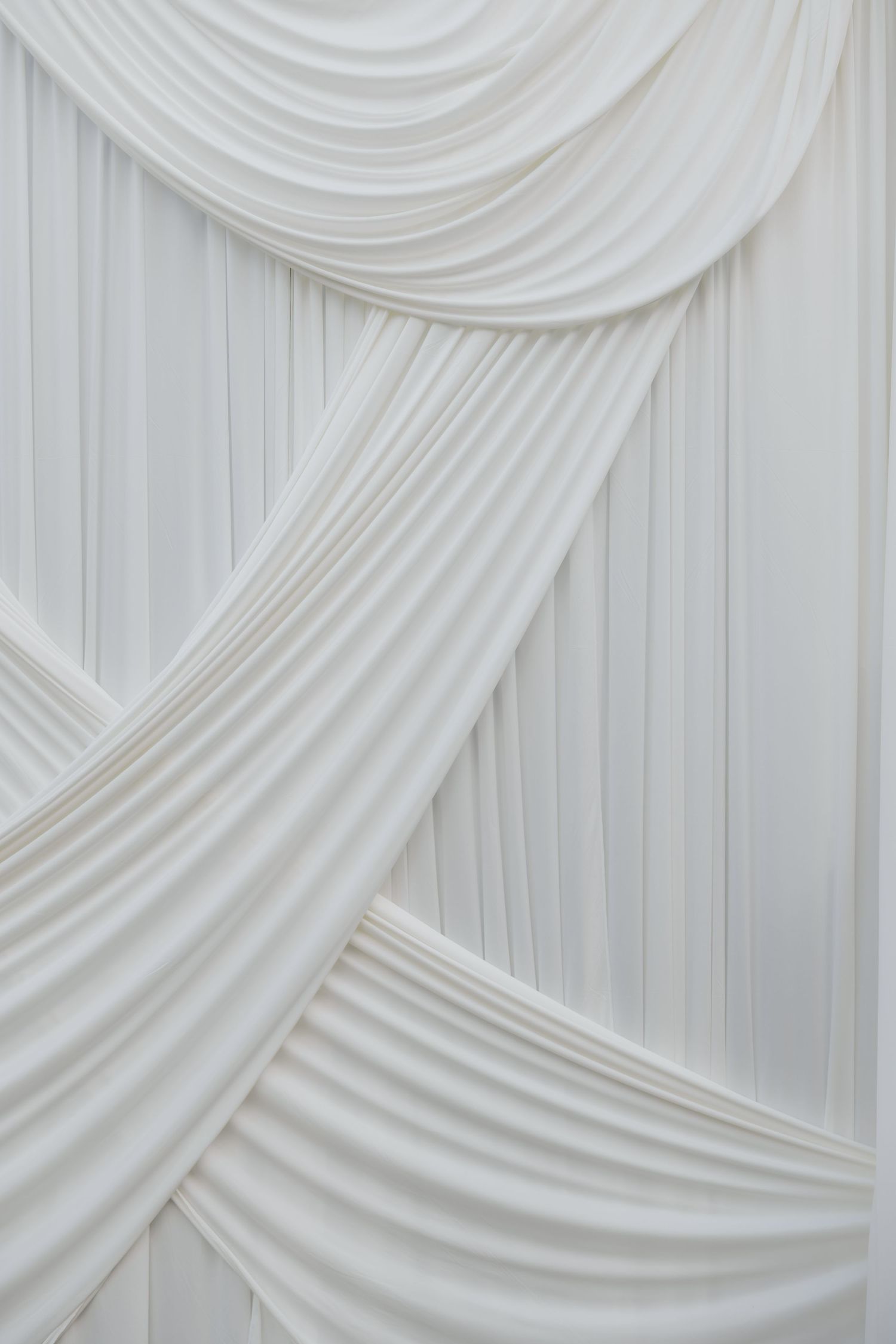 Elegant white draped fabric curtains arranged in graceful swags and pleats creating a luxurious decorative backdrop.