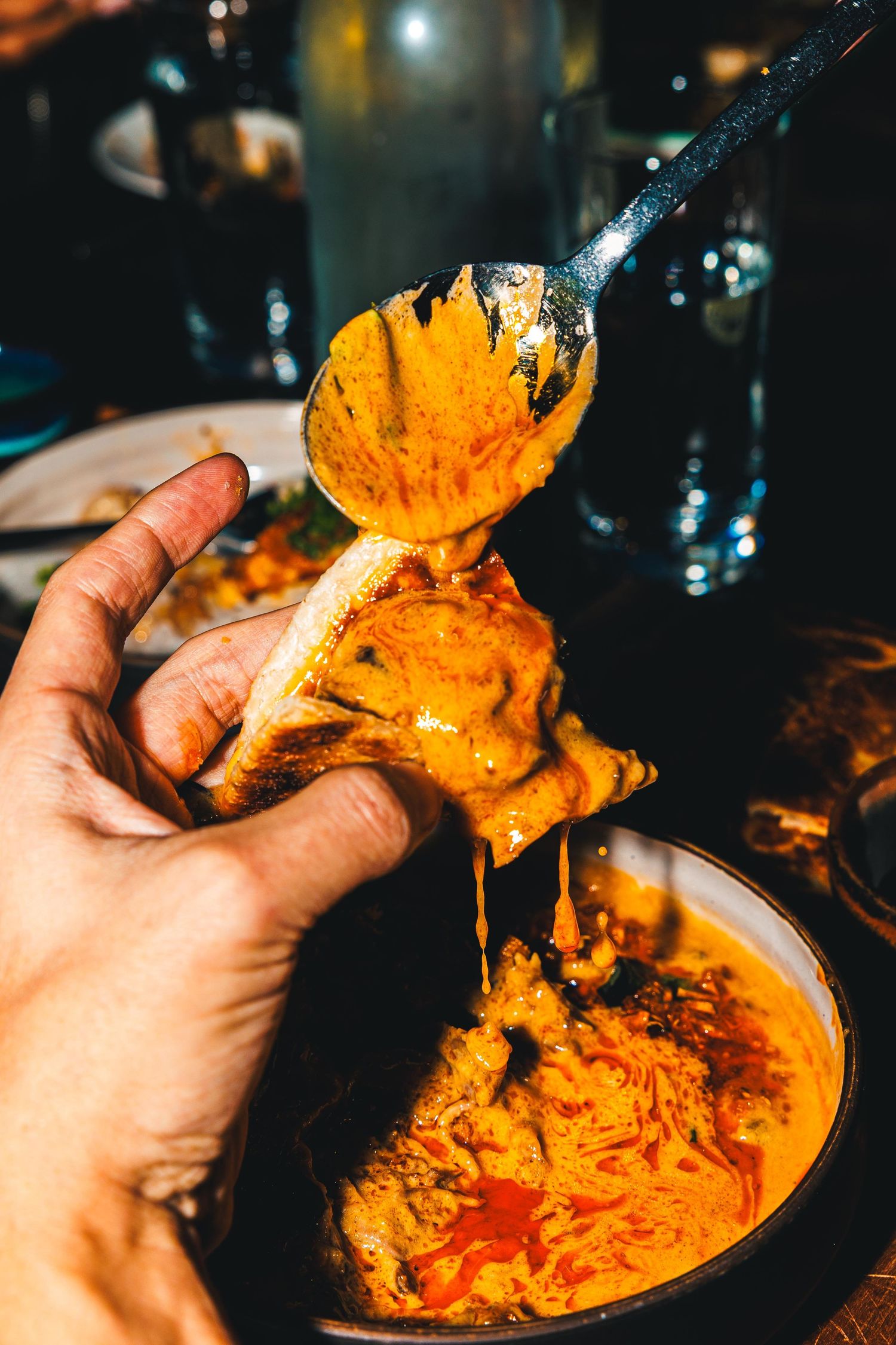 Scooping vibrant orange curry sauce with a spoon showing its rich and creamy texture.