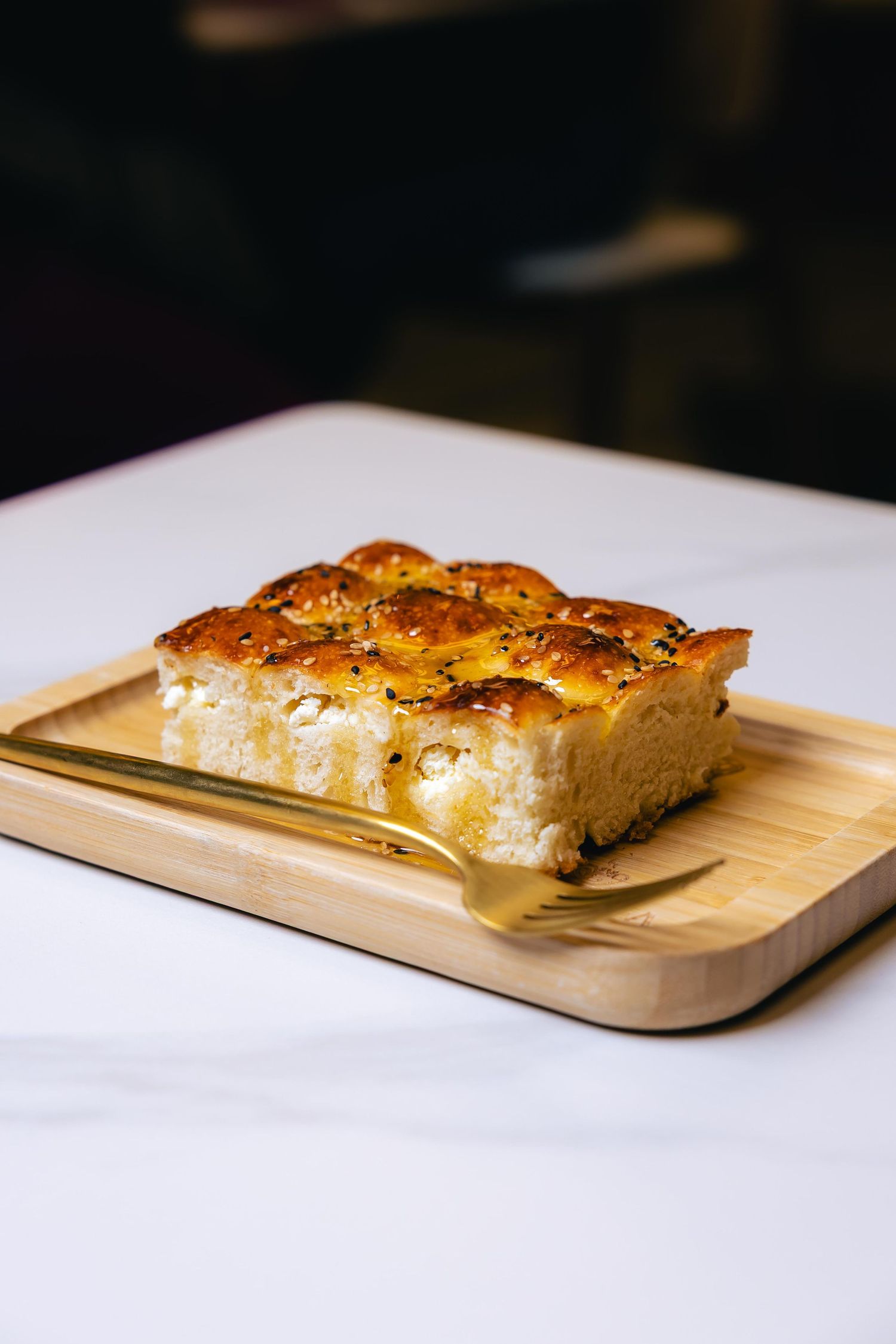Four sequential shots of a golden-brown focaccia bread on a wooden cutting board against a white background.