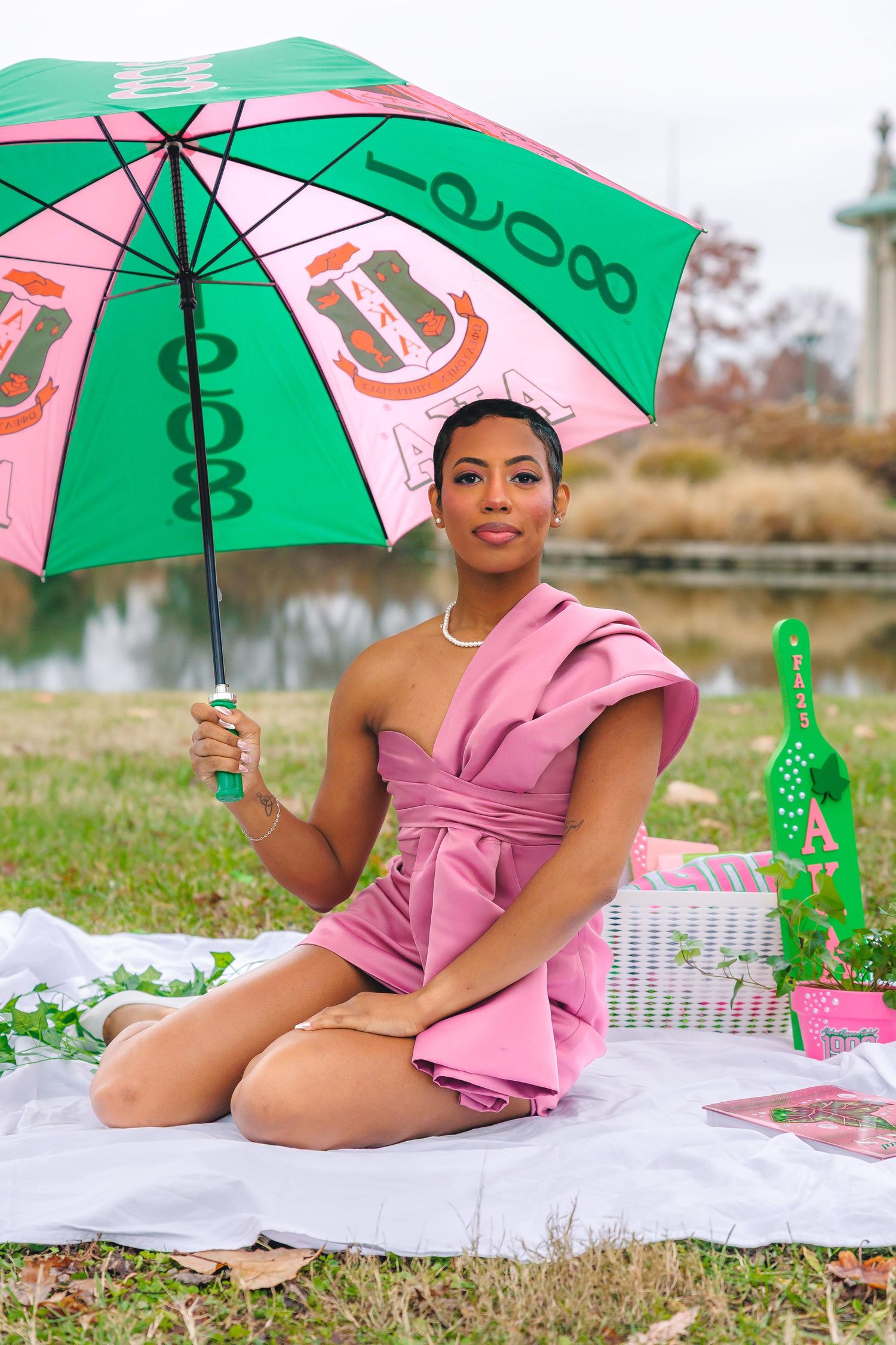 A picnic setup with green umbrella, pink outfit, and decorative accessories on grass.