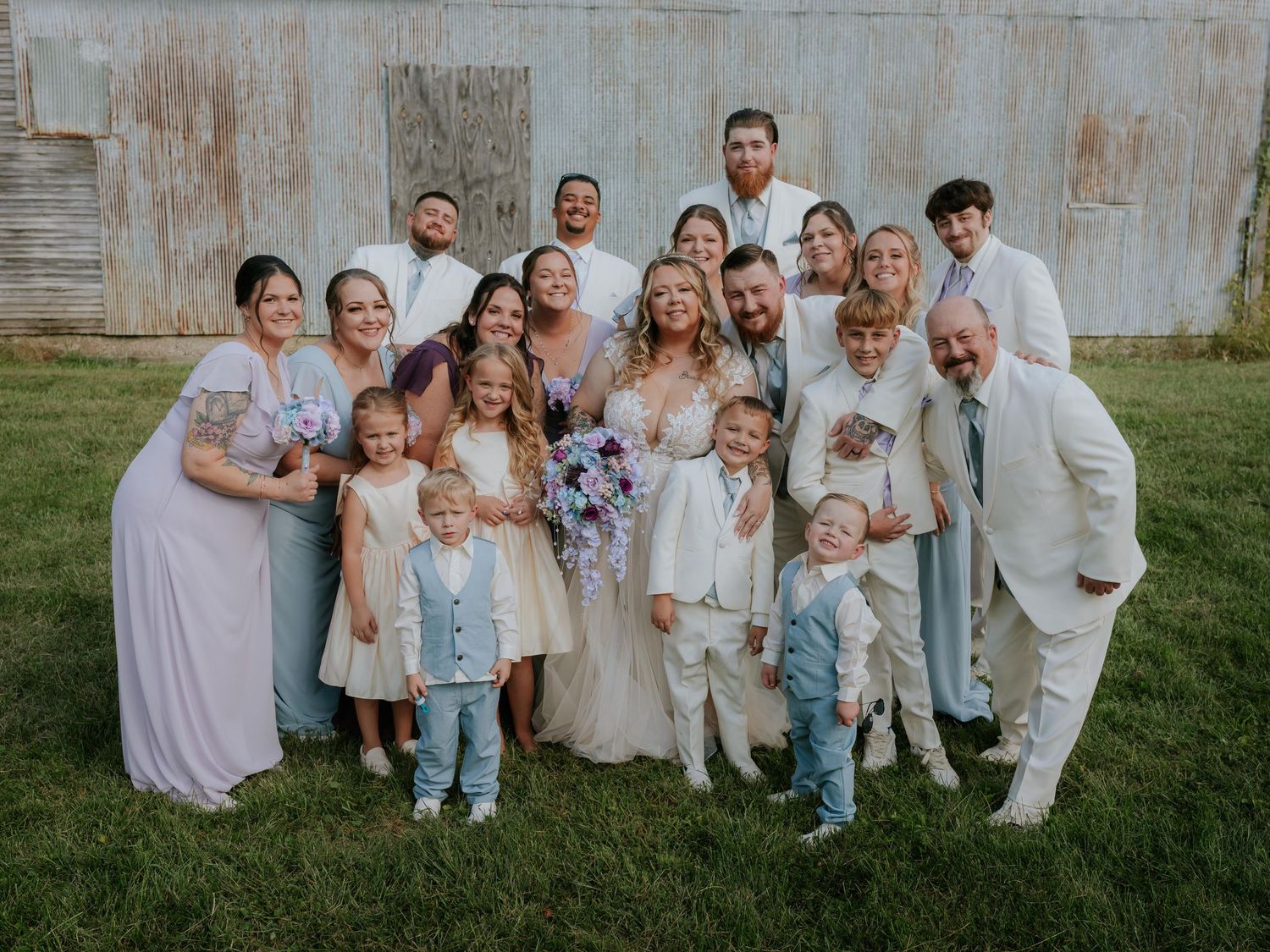Large family group photo against rustic barn wall outdoors at a wedding in St. Louis.