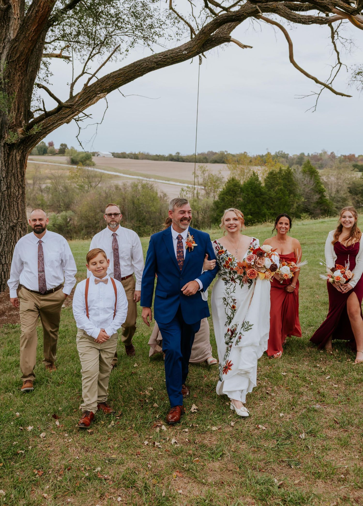 Wedding party poses playfully under a large tree in a rustic outdoor setting in Missouri.