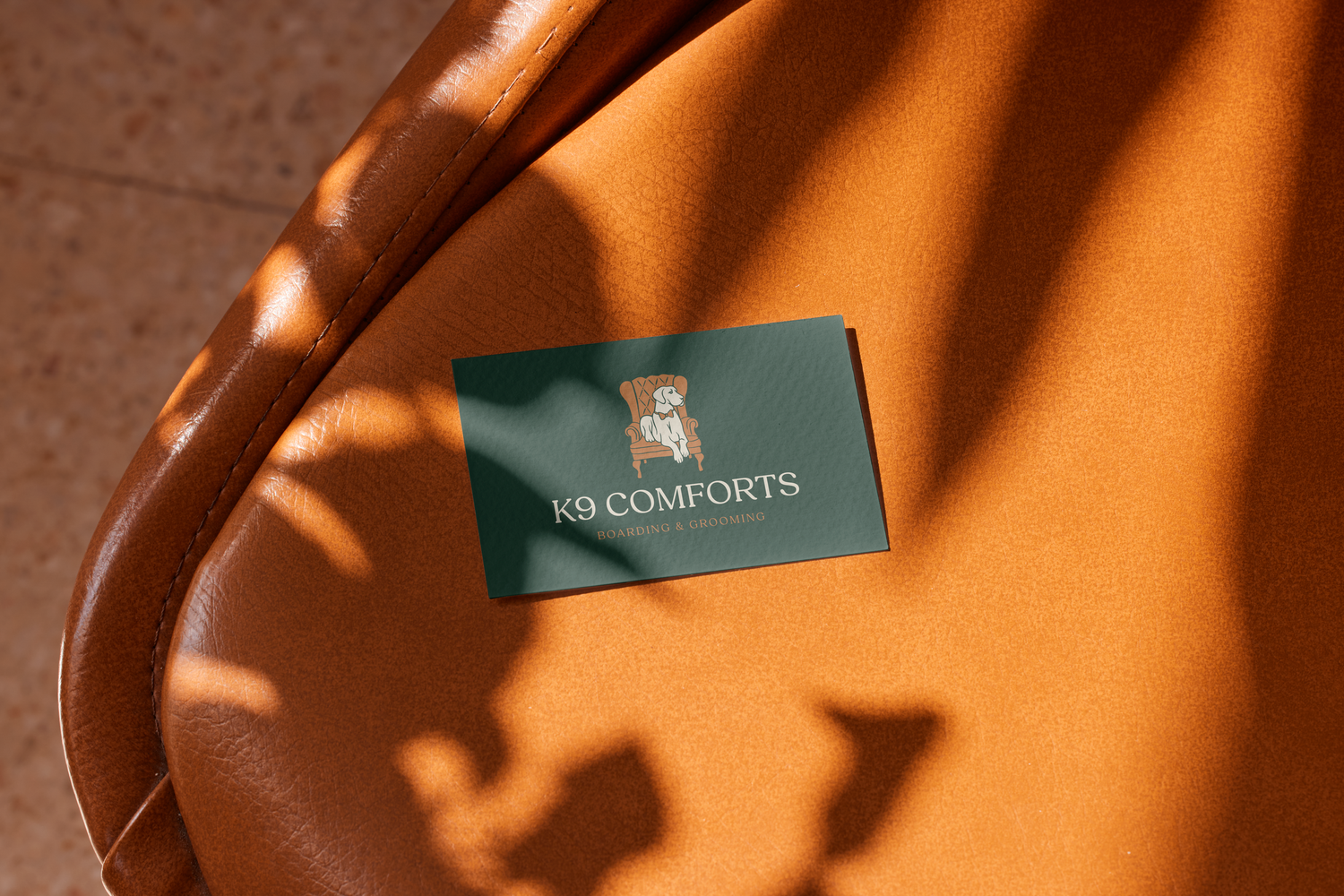 K9 Comforts branded business card resting on a tan leather surface with warm sunlight and leaf shadows.