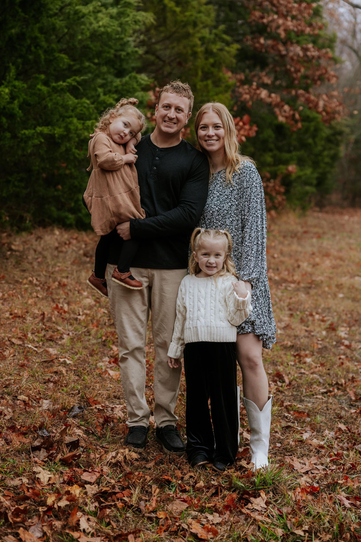A family poses together on fallen autumn leaves during an outdoor photo session.