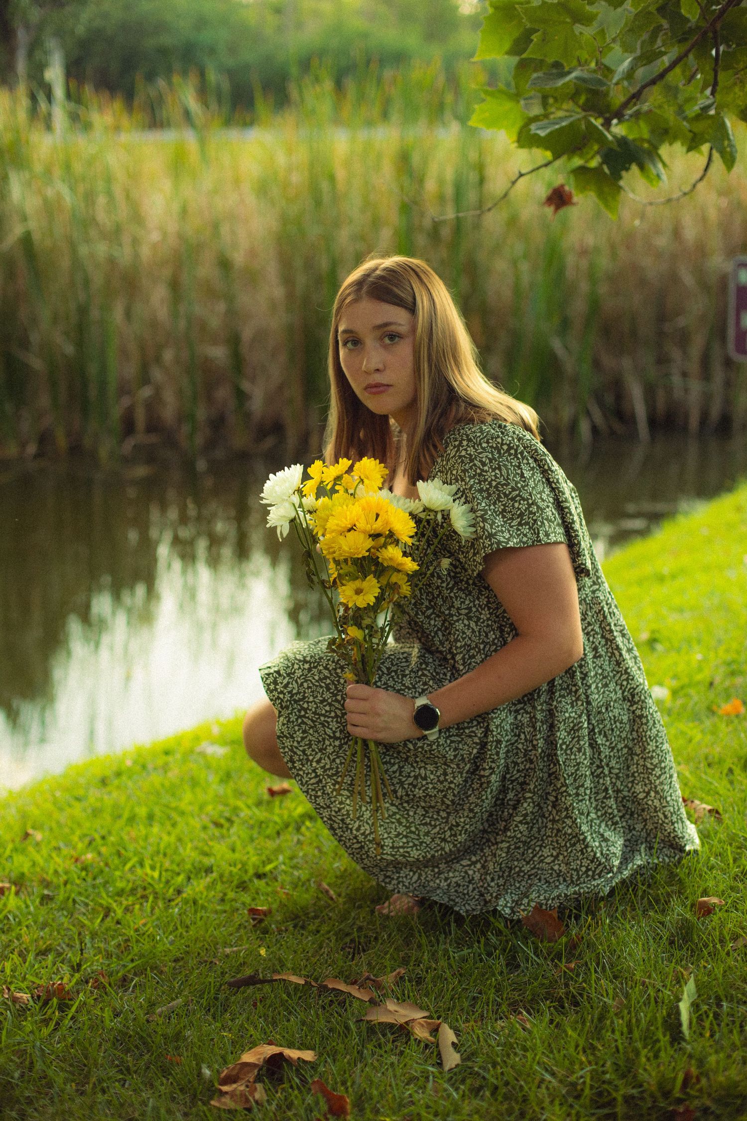 A portrait of a girl in a floral dress holds yellow flowers by a pond in golden evening light in Chesterfield, Mo.