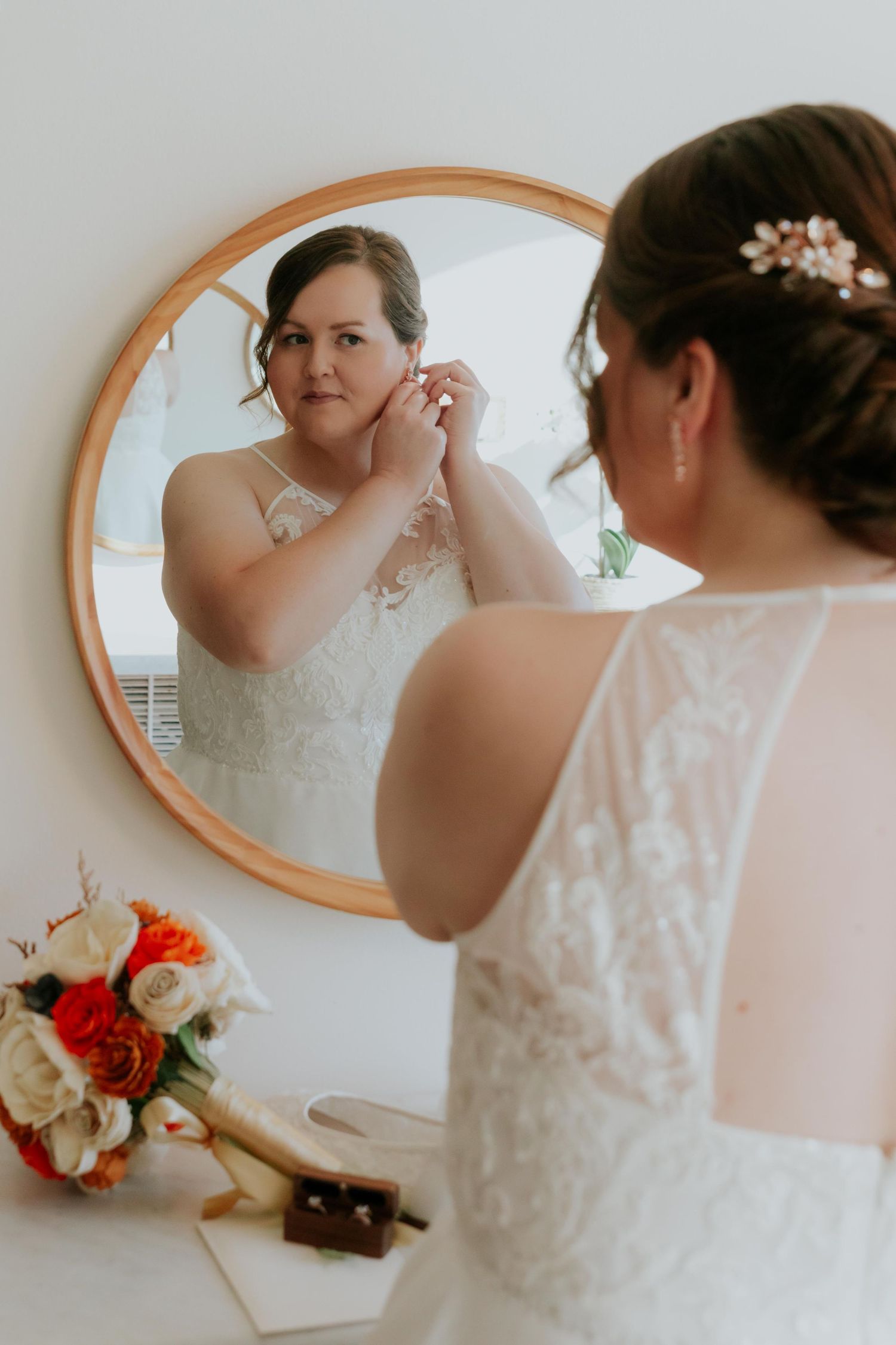 Wedding dress details and accessories reflected in an oval mirror with red flowers.