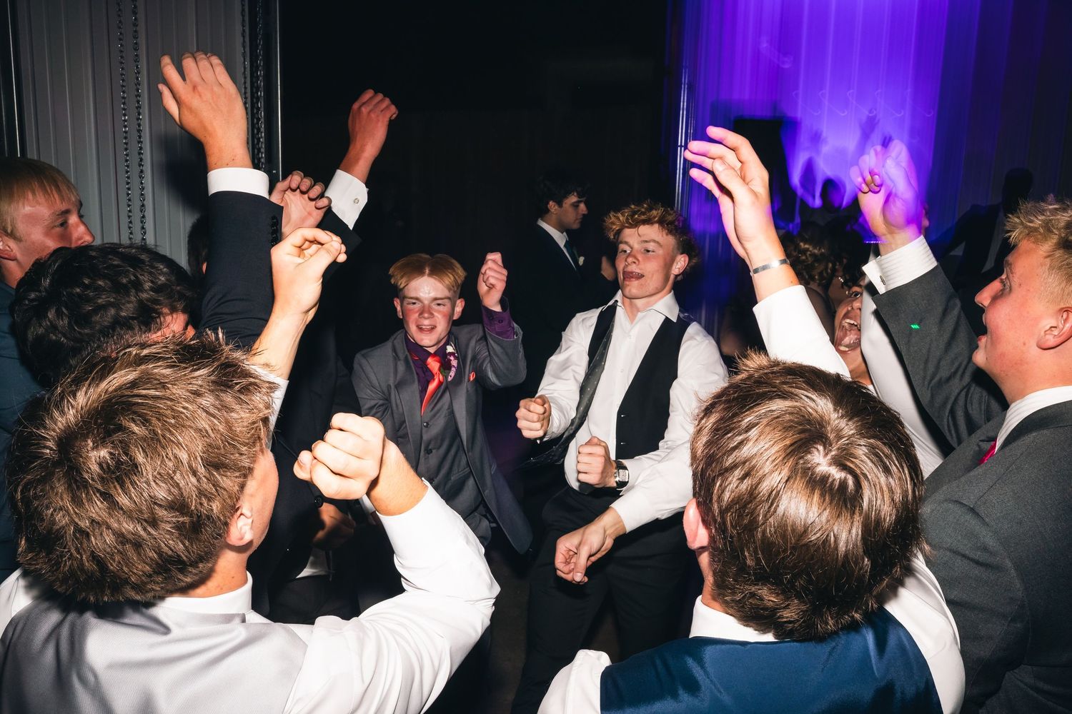 Energetic party crowd jumping and celebrating with hands in the air at a nighttime event.