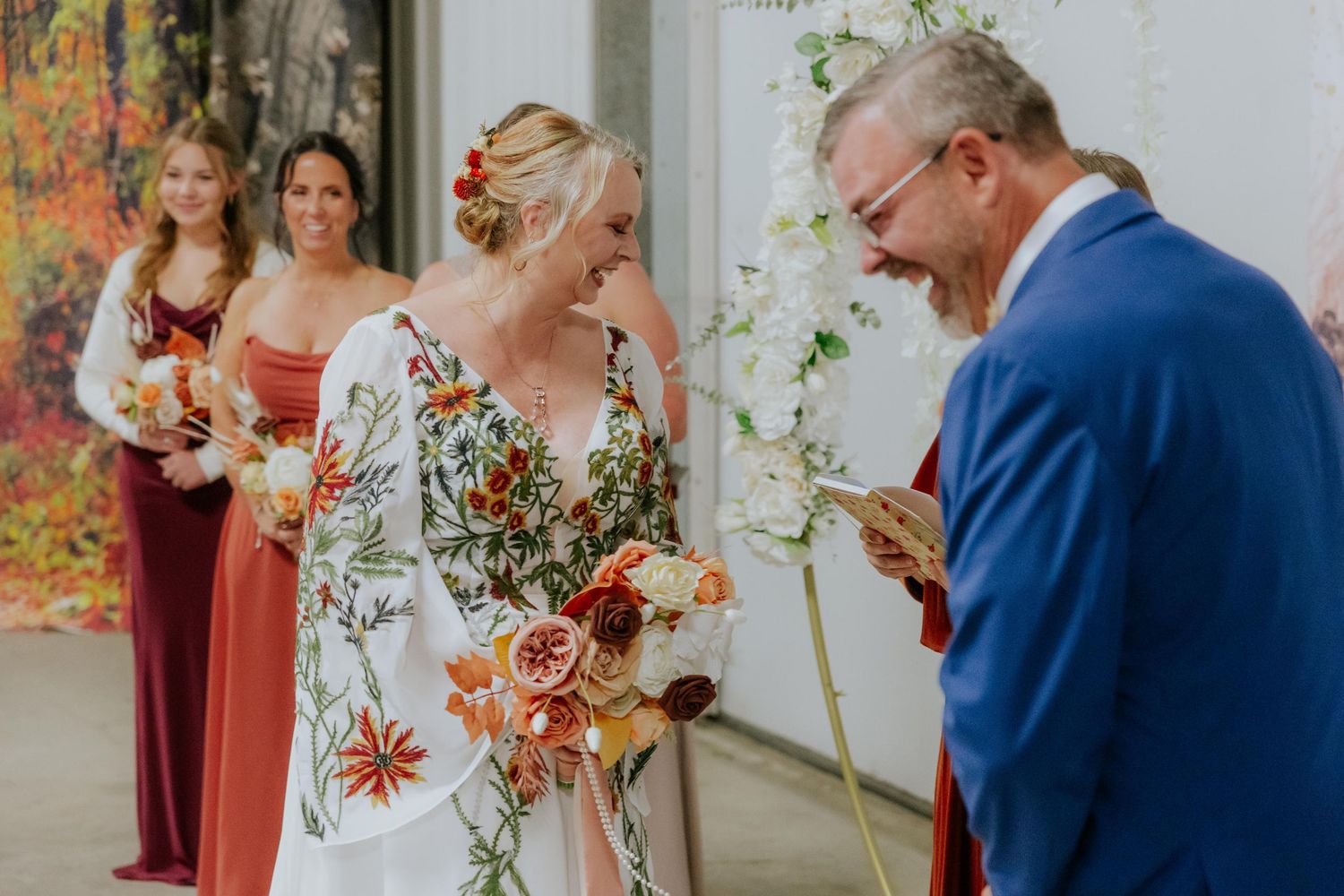 A wedding ceremony moment with a bride in floral dress and attendants in burgundy dresses.