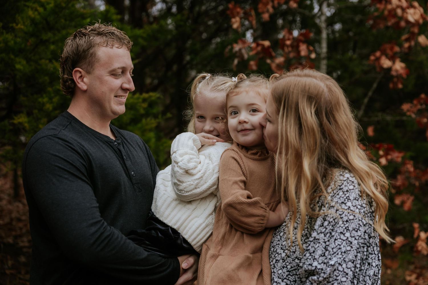 A family enjoys a playful autumn photoshoot together among fallen leaves in an outdoor setting.